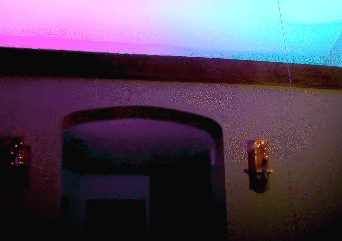 Ceiling displays a gradient of purple to blue light from LED strips. Wall sconces are illuminated with small lights.